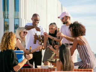 happy diverse friends clinking bottles on terrace