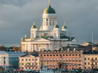 Auringonvalossa veden äärellä seisova katedraali, rauhallinen näky Helsingissä.