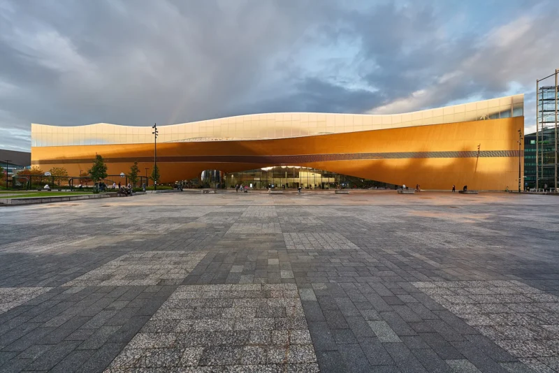 Oodi-kirjaston mutkitteleva puujulkisivu auringonlaskussa, edessä laaja kivetty aukio.