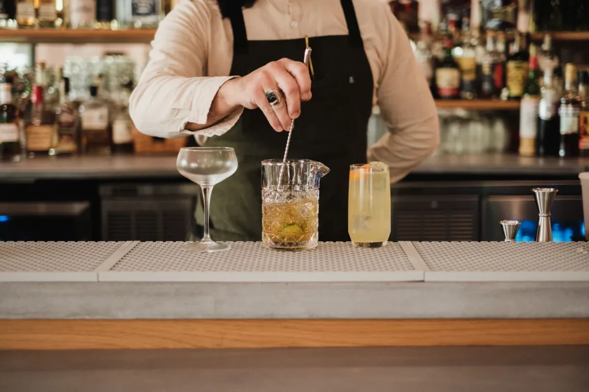 Baarimestari sekoittaa cocktailia baaritiskillä pullohyllyjen edessä