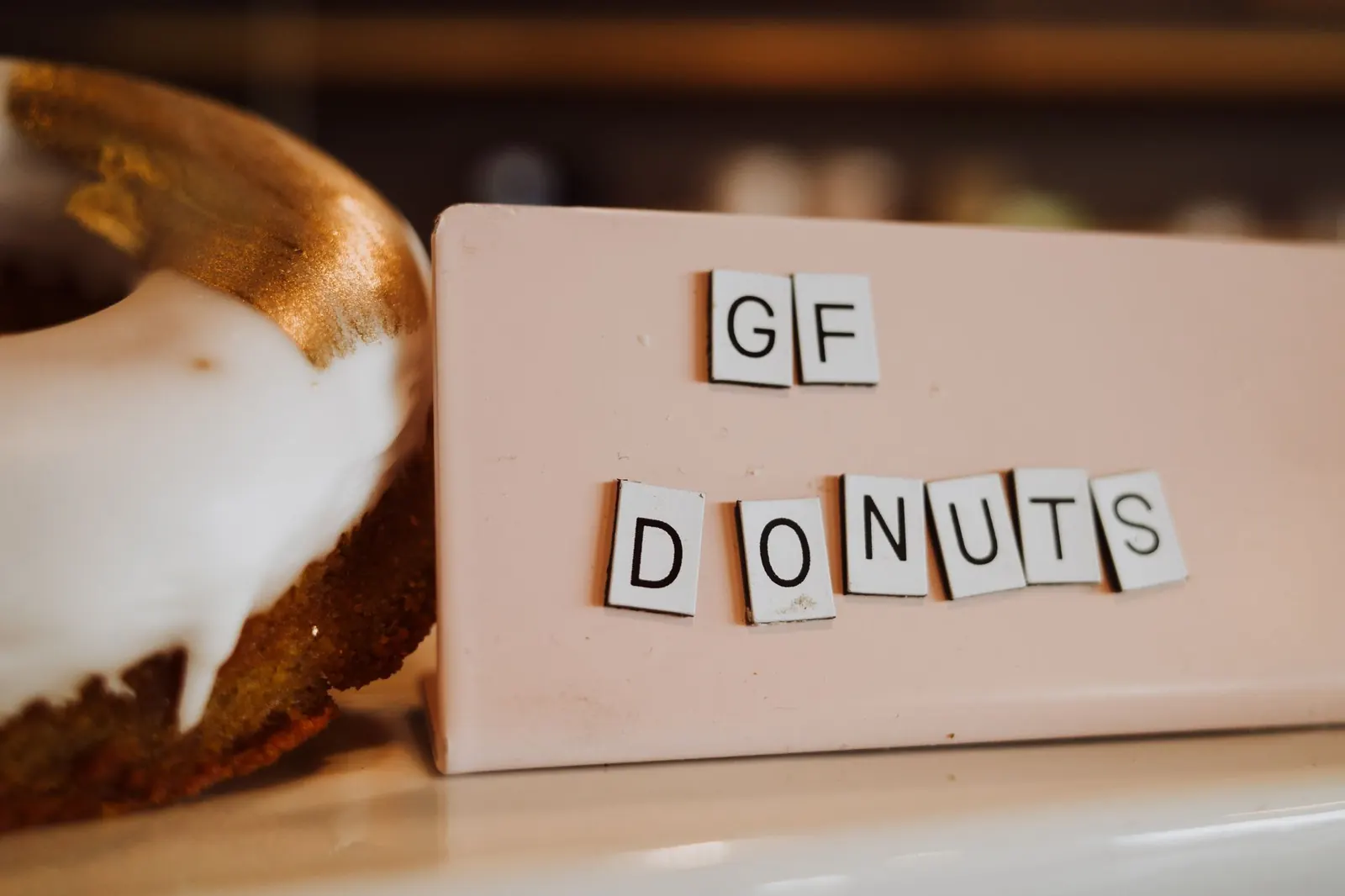 Gluteeniton donitsi valkoisella kuorrutteella ja GF DONUTS -kyltti kahvilan tiskillä