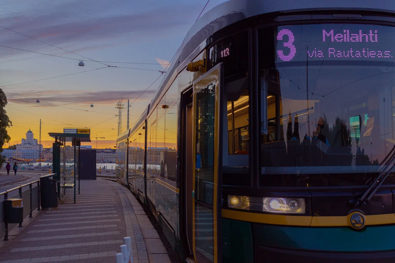 Helsingin ratikka 3 pysäkillä auringonlaskussa, taustalla tuomiokirkko