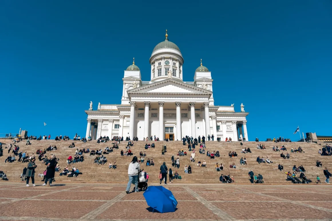 Helsingin tuomiokirkko ja portaille istahtaneita ihmisiä kirkkaansinisen taivaan alla