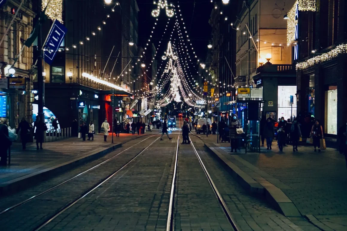 Joulukoristeiden valaisema Helsingin keskusta illalla, raitiovaunukiskot ja jalankulkijoita kadulla