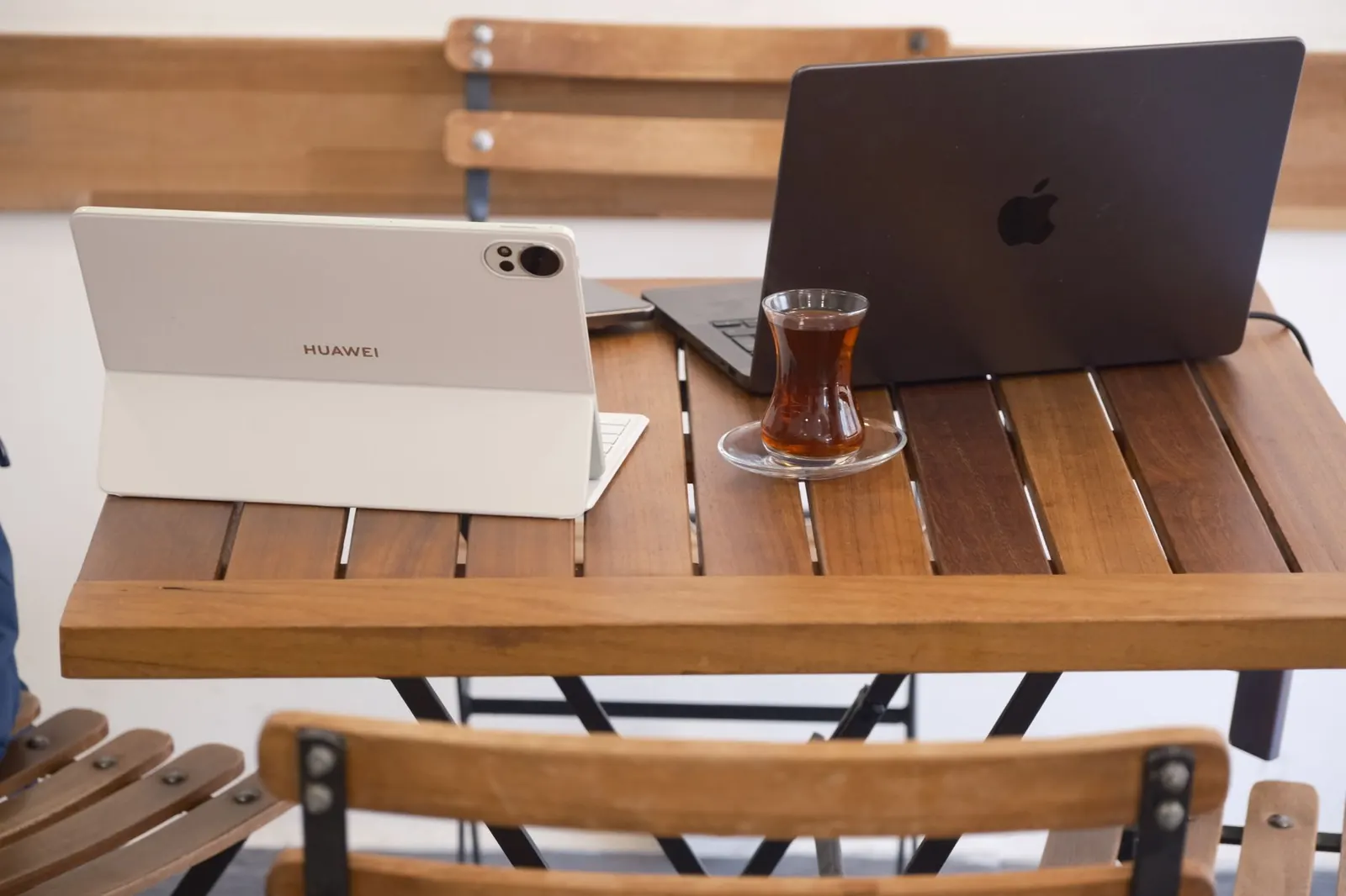 Kahvilapöydällä kannettava tietokone, tabletti ja lasillinen teetä