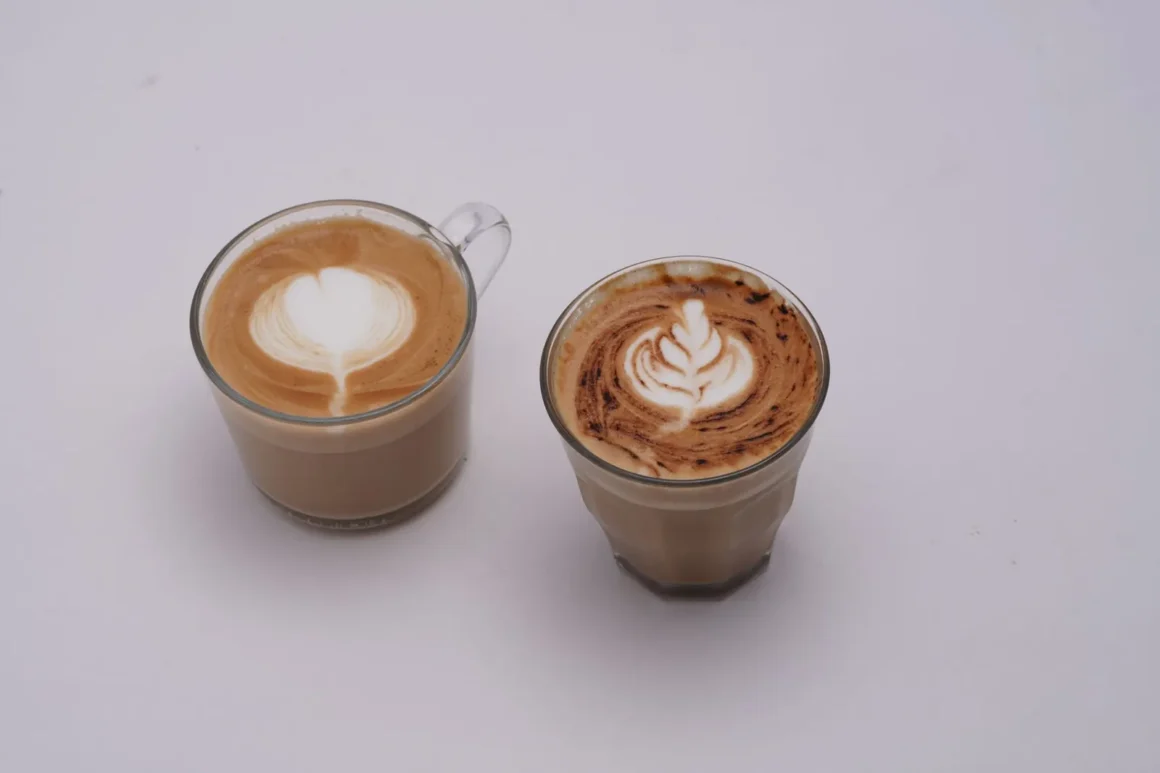 Kaksi lasikuppia latte-taiteella koristeltua kahvia valkoisella taustalla