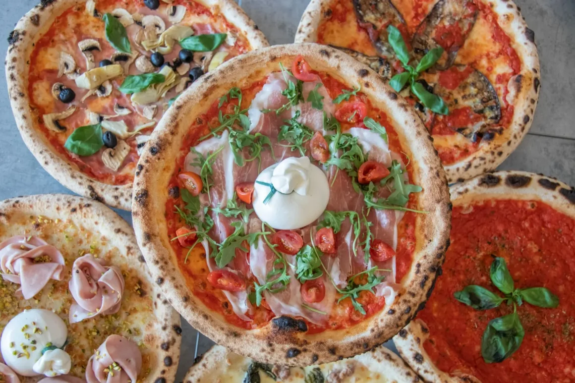 Kimppu napolilaistyylisiä pizzoja ylhäältä kuvattuna, päällä pršuttoa, burrataa, tomaattia ja rucolaa