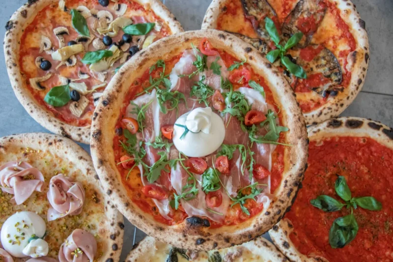 Kimppu napolilaistyylisiä pizzoja ylhäältä kuvattuna, päällä pršuttoa, burrataa, tomaattia ja rucolaa