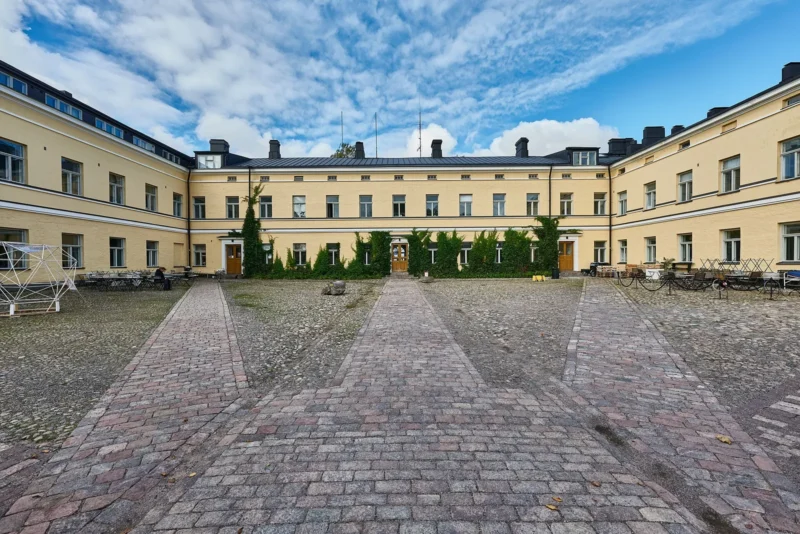 Lapinlahden vanhan sairaalan keltainen päärakennus ja kivetty sisäpiha kahvilapöytineen