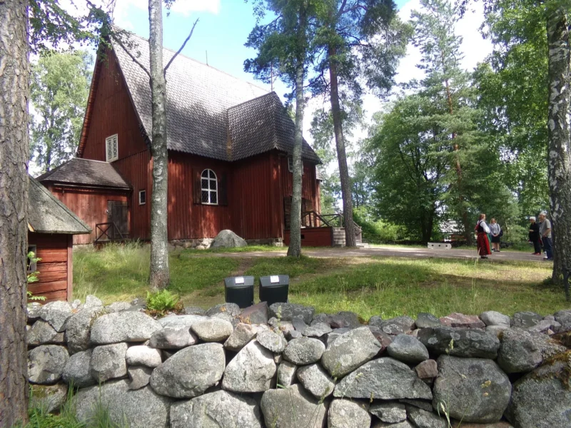 Punainen puinen Karunan kirkko mäntyjen ja kivimuurin takana Seurasaaren ulkomuseossa