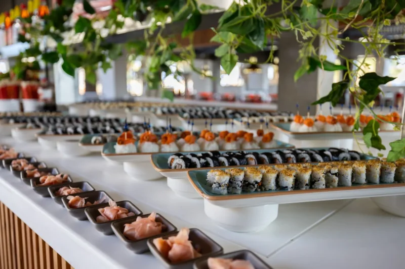 Sushibuffetin tarjoilupöytä, jolla on rivejä sushirullia ja lohipaloja vadeilla