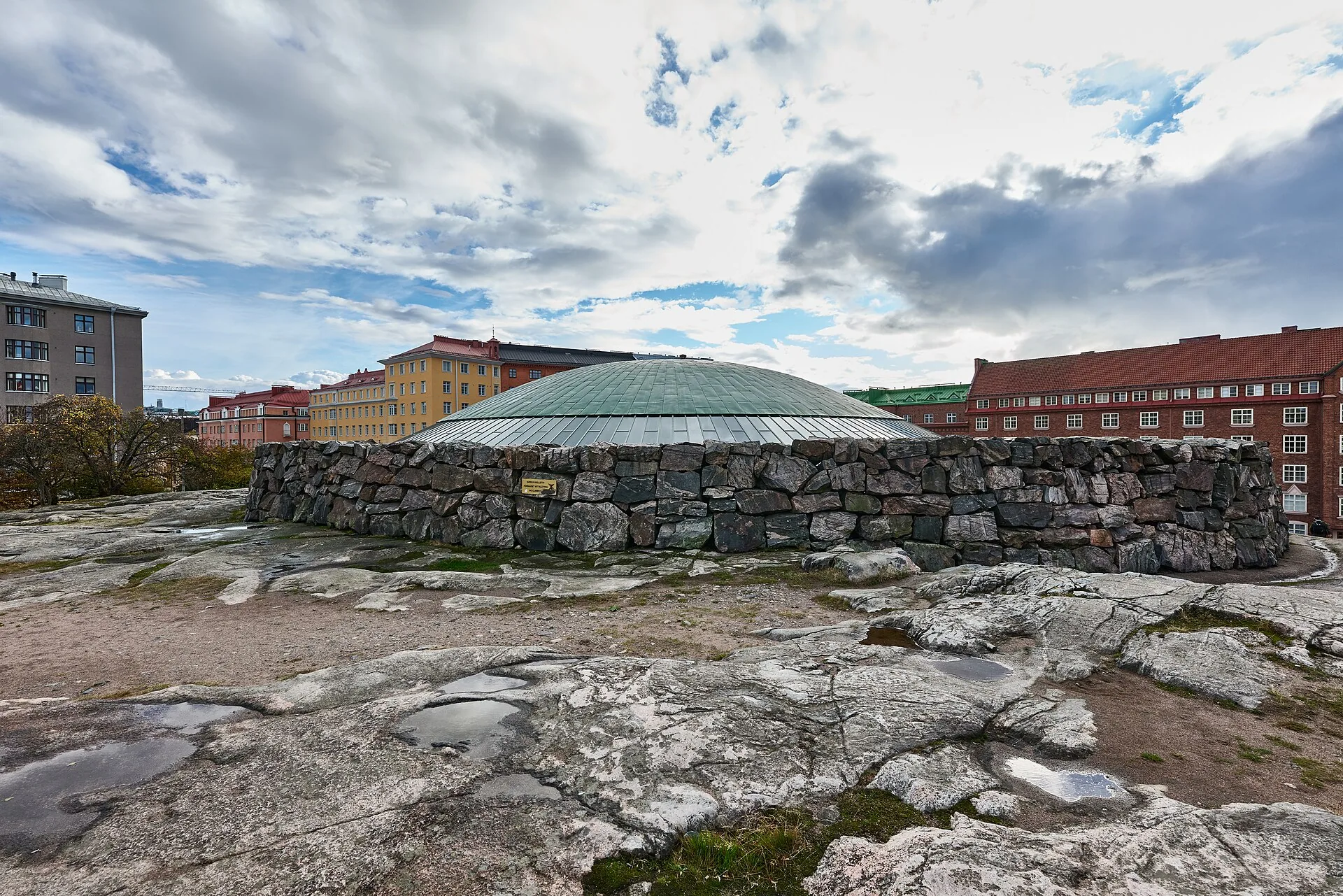 Temppeliaukion kirkon kupoli ja karkea kiviseinä kallion päällä, taustalla Helsingin kerrostaloja