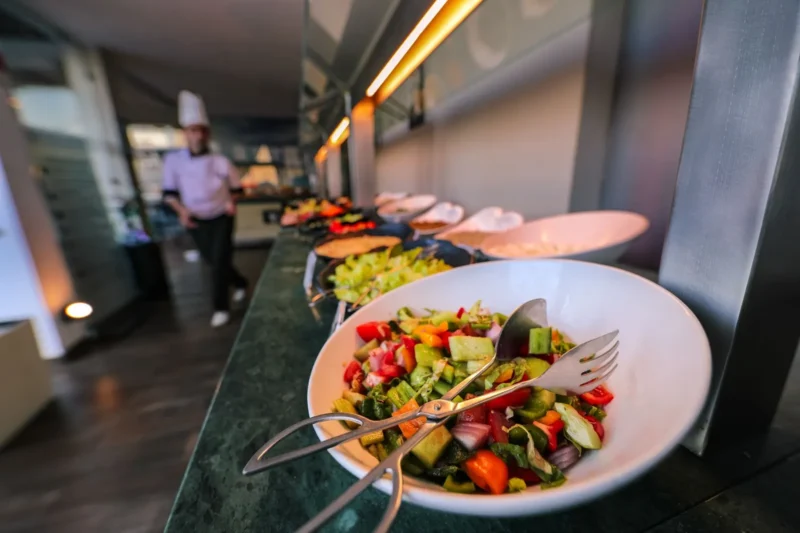 Värikäs salaatti lounasbuffetin edessä, taustalla kokki