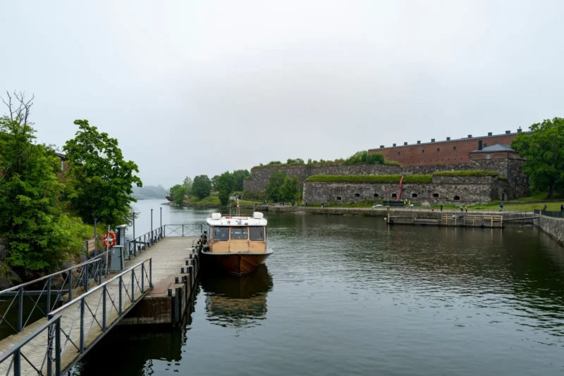 Vene Suomenlinnan satamalaiturilla ja linnoituksen muureja pilvisenä päivänä